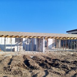 BM PROFIT - Wznoszenie ścian budynku z betonu komórkowego, widoczne podpory stropu i szalunki, przygotowanie do zalewania betonem.