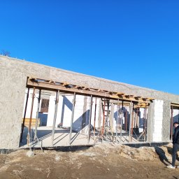 BM PROFIT - Budowa domu z betonu komórkowego: ściany wzniesione, widoczne podpory szalunkowe, teren wokół budynku w stanie surowym.