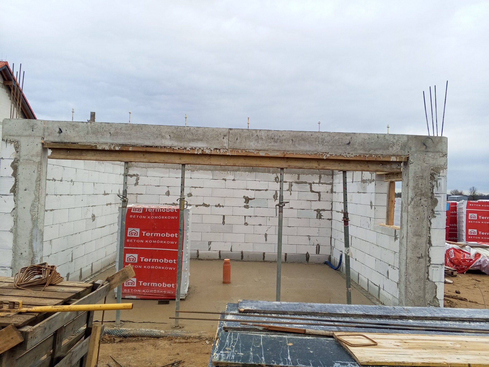 Wznoszenie ścian z betonu komórkowego Termobet, widoczne podpory stropowe i zbrojenie pionowe, elementy szalunku w tle, budowa w trakcie realizacji.
