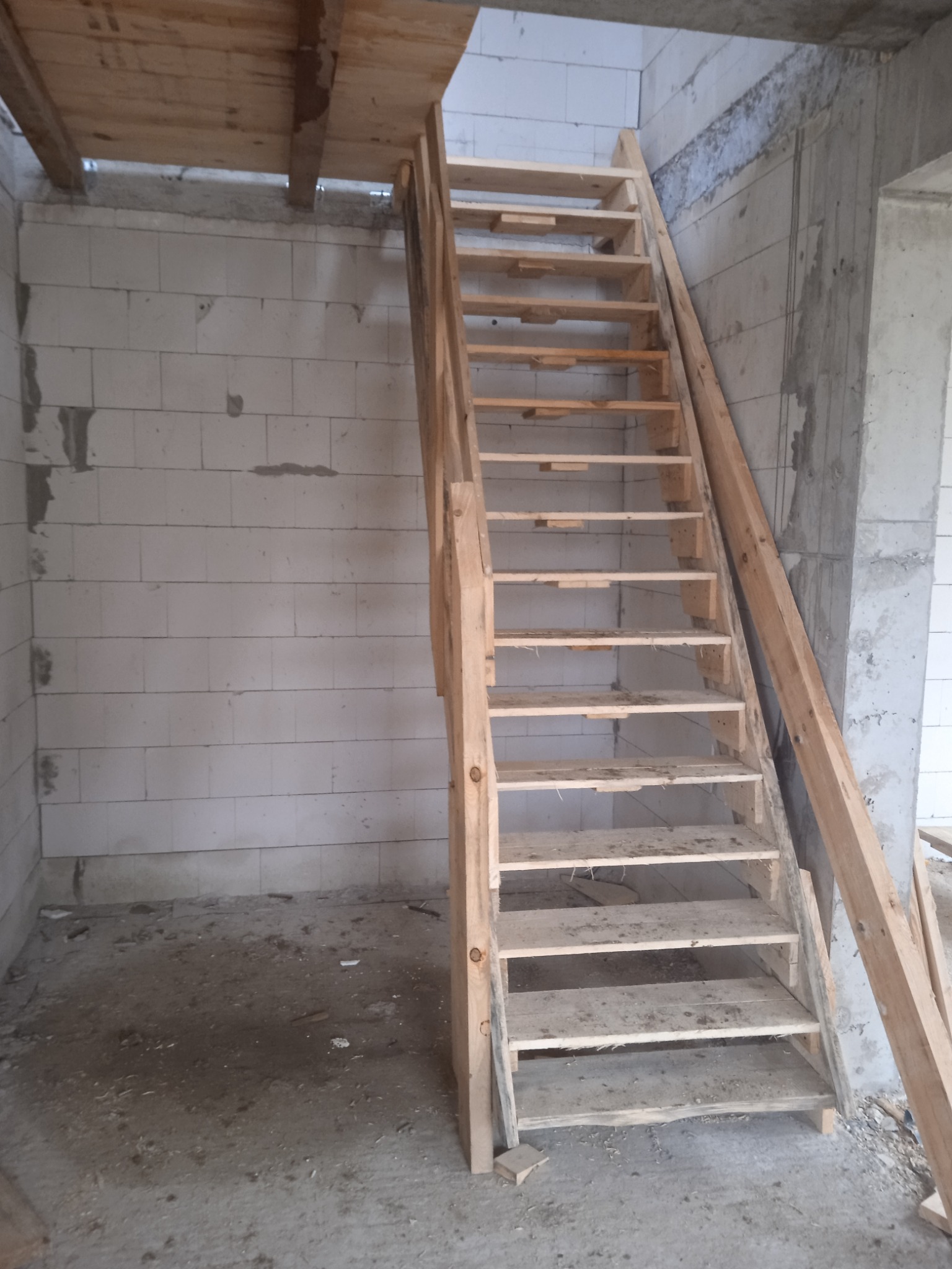 Surowe drewniane schody tymczasowe w surowym stanie, w trakcie budowy domu z bloczków betonowych, z widoczną konstrukcją stropu.