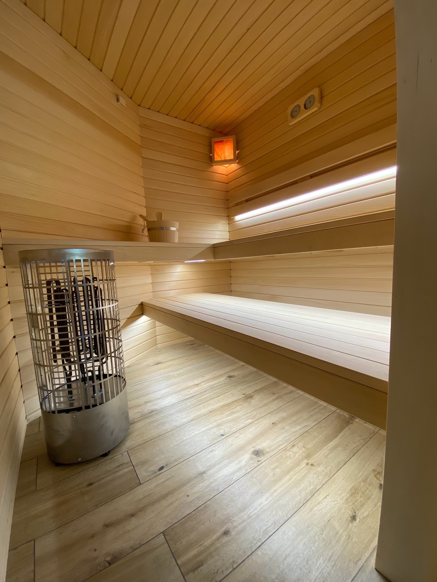 Jasne drewno w saunie: piec, ławy, oświetlenie LED i akcesoria. Ujęcie z niskiego kąta podkreśla przestrzeń i detale wykończenia.