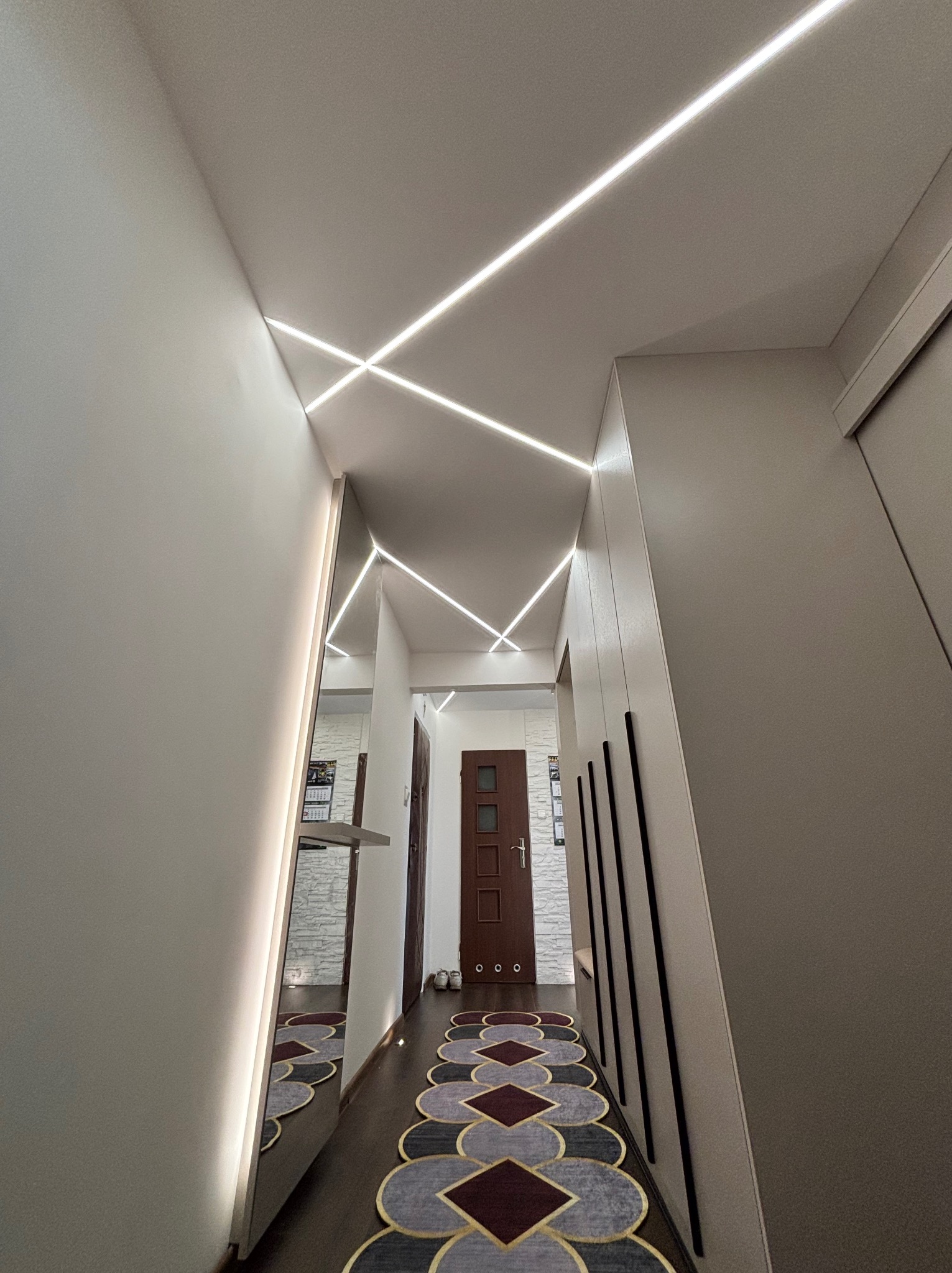 Nowoczesne oświetlenie LED w przedpokoju w Wąbrzeźnie. Geometryczne linie światła na suficie, lustro z podświetleniem i dywan w geometryczne wzory.
