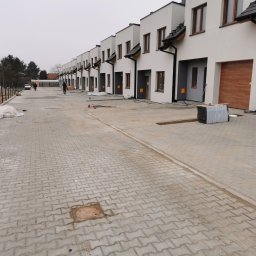 FAVOR - ANDRII SKLIAR - Nowe osiedle domów szeregowych z wybrukowaną drogą dojazdową. Kostka brukowa ułożona w zygzak. Widoczne studzienki kanalizacyjne i przygotowane materiały budowlane.