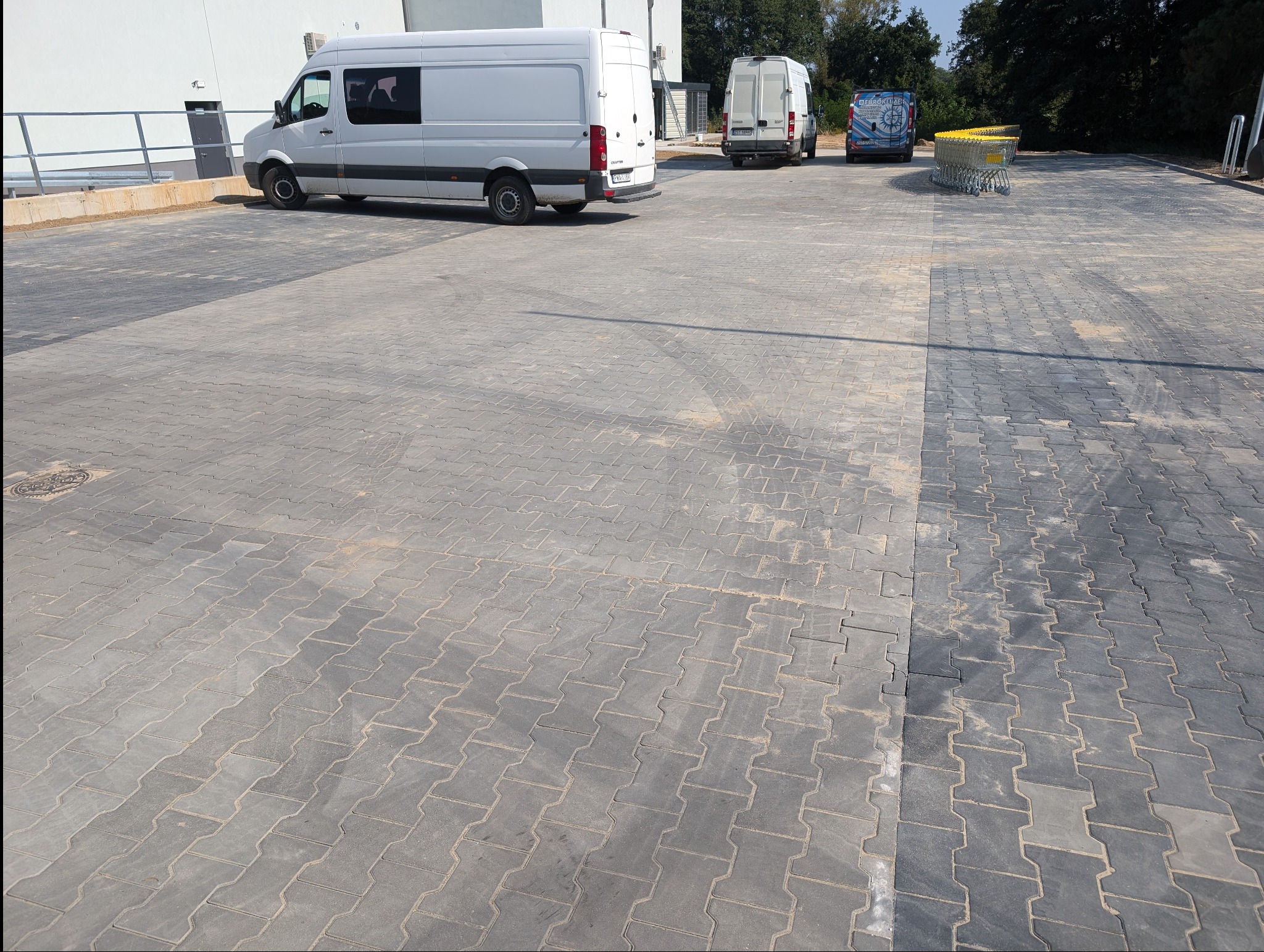 Szara kostka brukowa typu I na parkingu z białymi busami w tle. Widoczny fragment czyszczonej powierzchni. Ułożona równo, z zachowaniem wzoru.