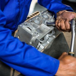 Nica Serwis - Silnik samochodowy w trakcie montażu, dokręcanie śrub kluczem nasadowym, widoczny pracownik w niebieskim kombinezonie.