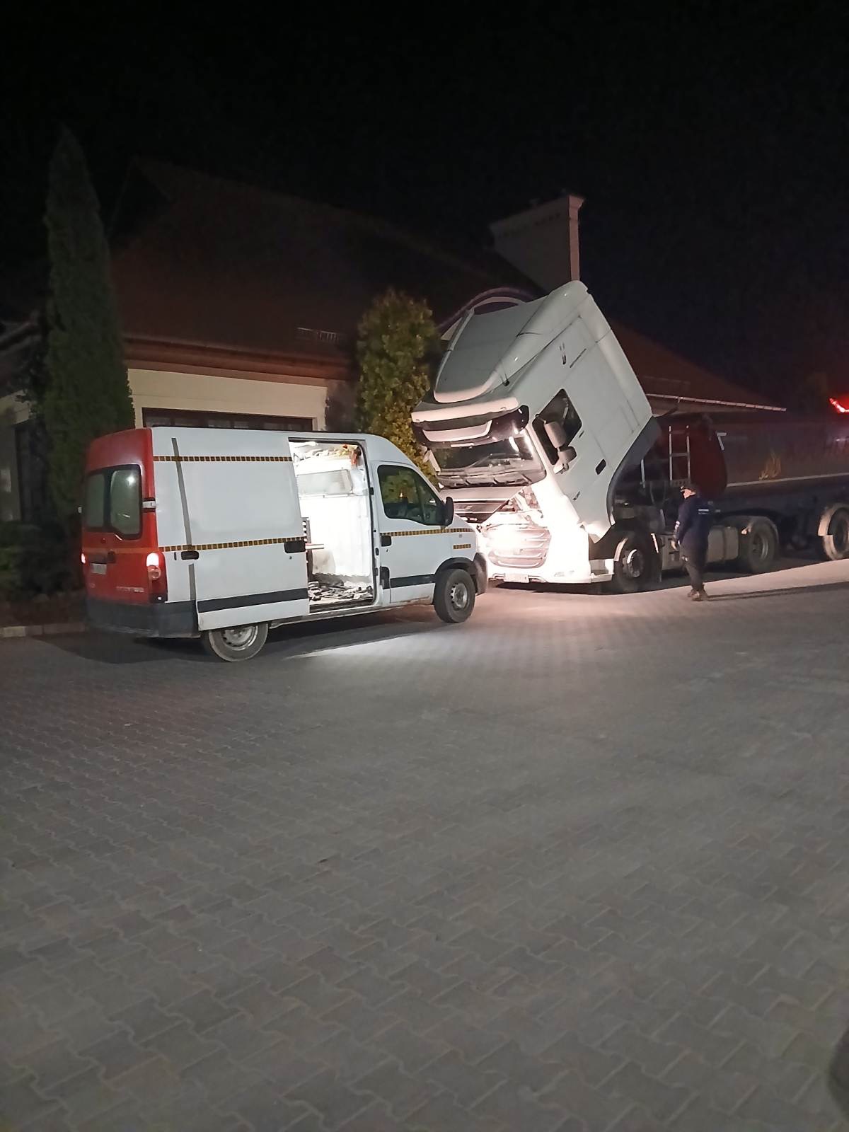 Awaryjna naprawa TIRa przy użyciu mobilnego warsztatu w nocy. Otwarty furgon serwisowy obok uniesionej kabiny ciężarówki oświetlonej od dołu.