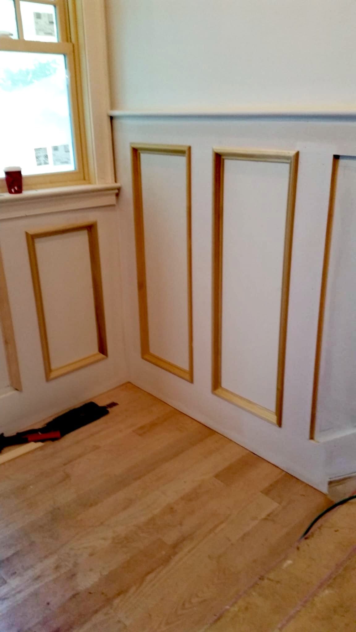 Ściana z dekoracyjnymi panelami i listwami w kolorze złota, drewniana podłoga, narzędzie do cięcia przy ścianie, widok z niskiego kąta.