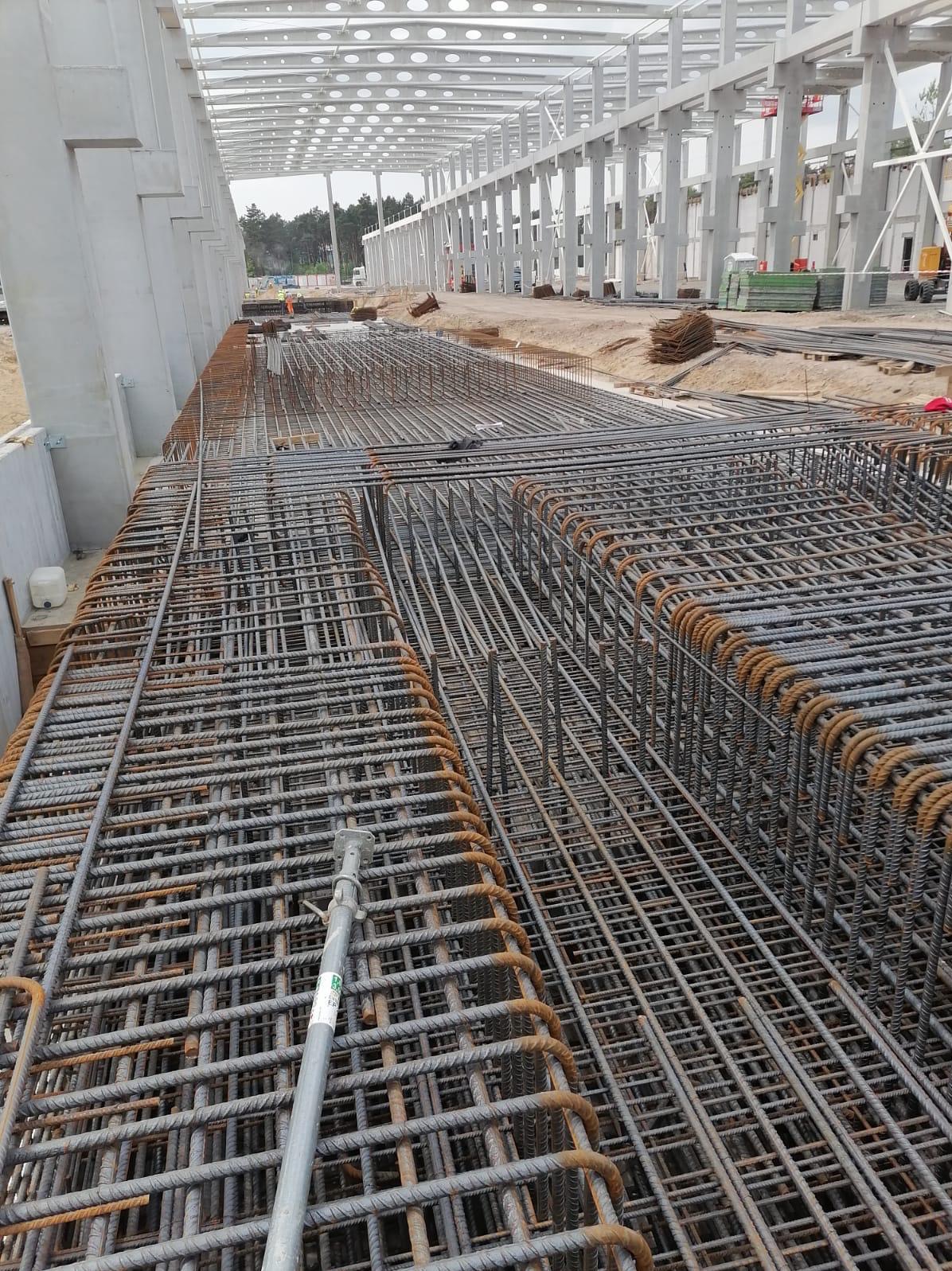 Siatka zbrojeniowa przygotowana pod wylewkę fundamentów hali, widoczne metalowe podpory i elementy konstrukcji stalowej dachu.