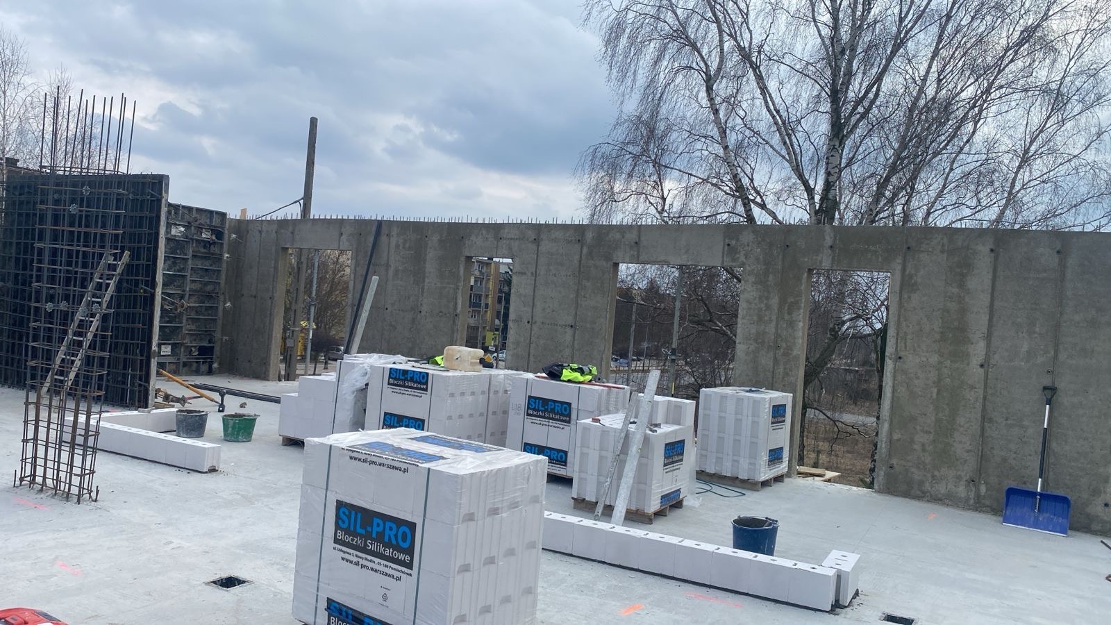 Wznoszenie ścian z betonu komórkowego Sil-Pro na budowie. Widoczne szalunki, zbrojenia i narzędzia. Surowy stan budynku w trakcie realizacji.