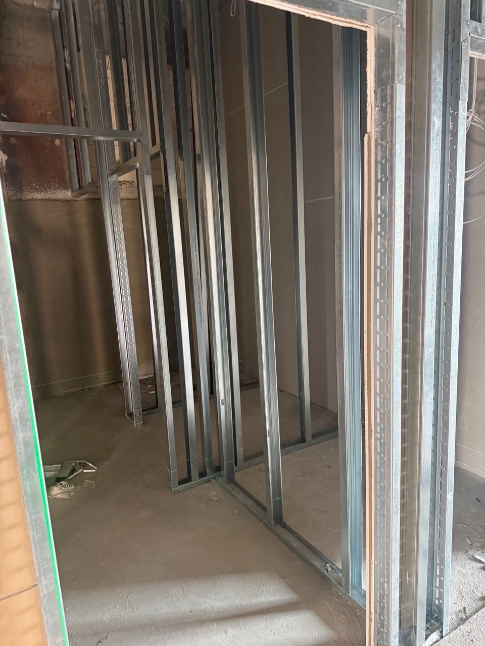 Metalowa konstrukcja szkieletowa ścian działowych w surowym wnętrzu. Widoczne profile i podłoże pod wylewkę. Etap budowy z bliska.