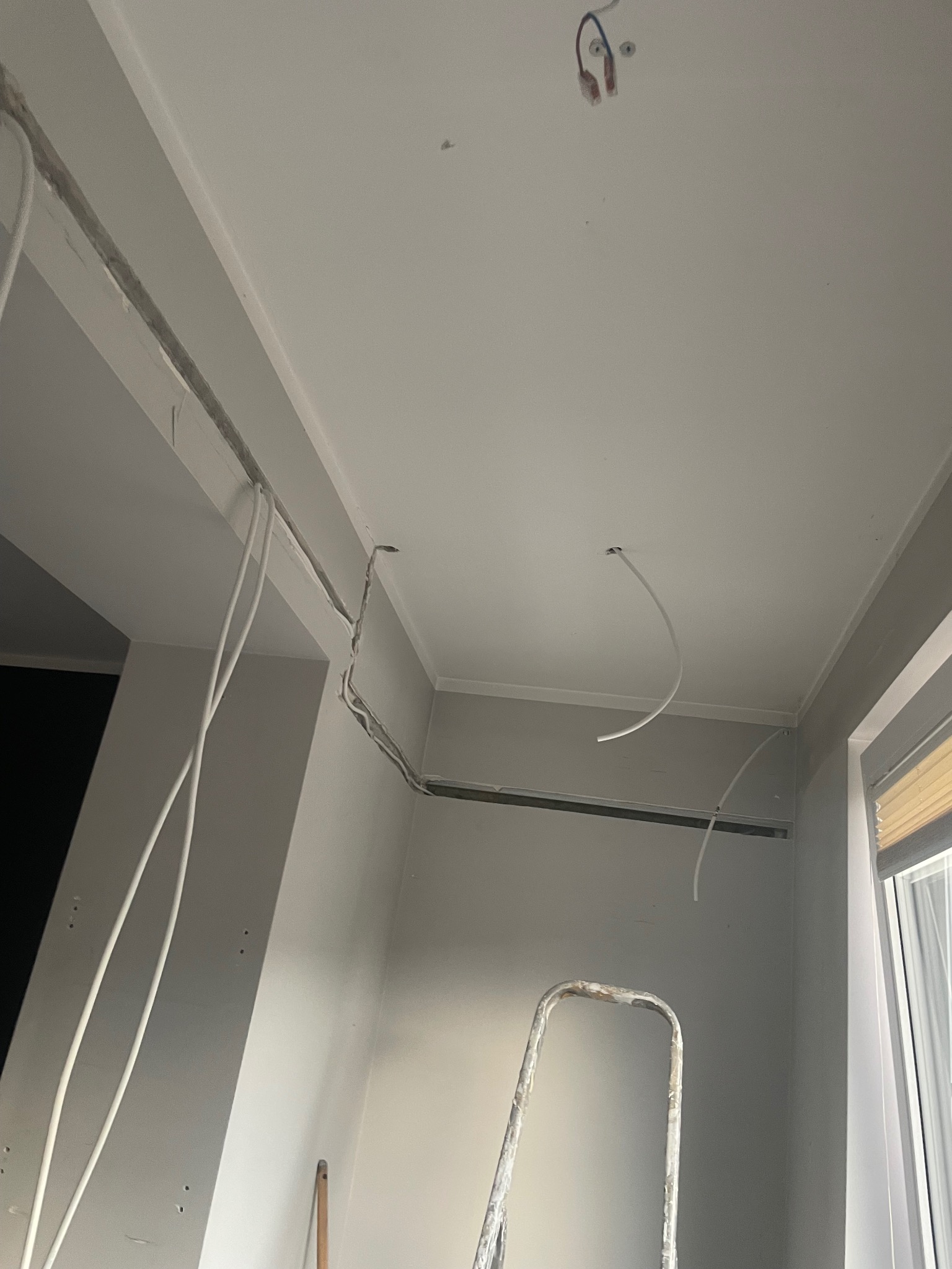 Białe przewody elektryczne w ścianie i suficie podczas prac w Grądy-Woniecko. Widoczna drabina malarska i okno.