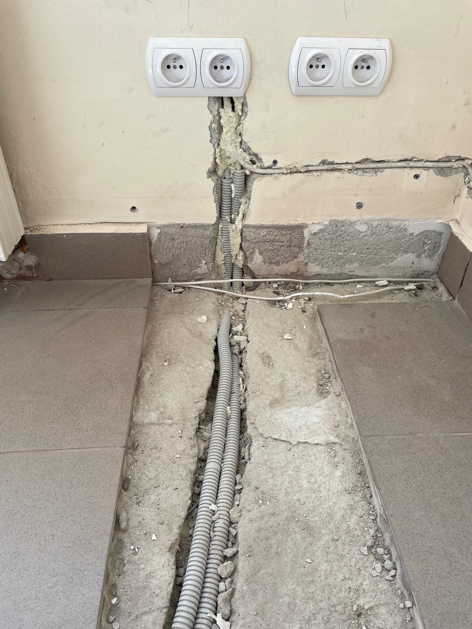 Bruzdy w ścianie i podłodze z ułożonymi rurami instalacji elektrycznej, przygotowane gniazdka elektryczne. Prace w toku.