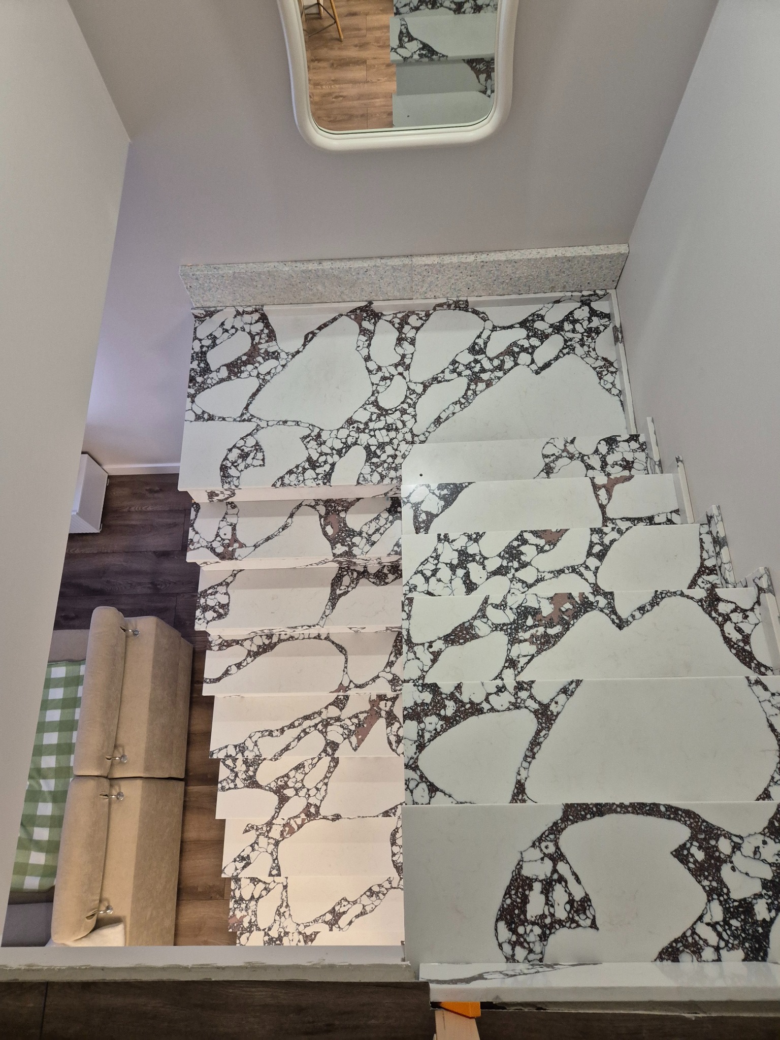 Białe schody z unikalnym wzorem marmuru, widok z góry, z odbiciem w lustrze. Nowoczesne wykończenie wnętrza, jasne ściany, minimalistyczny design.