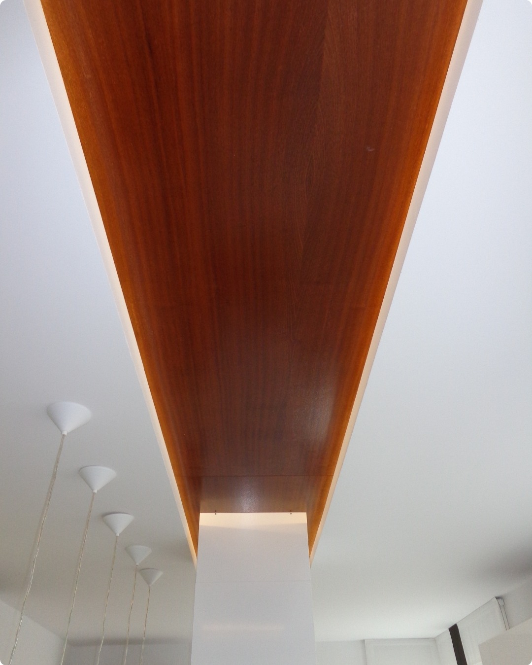 Drewniana belka sufitowa z oświetleniem LED, wkomponowana w biały sufit, widok z dołu, minimalistyczne lampy wiszące w tle.