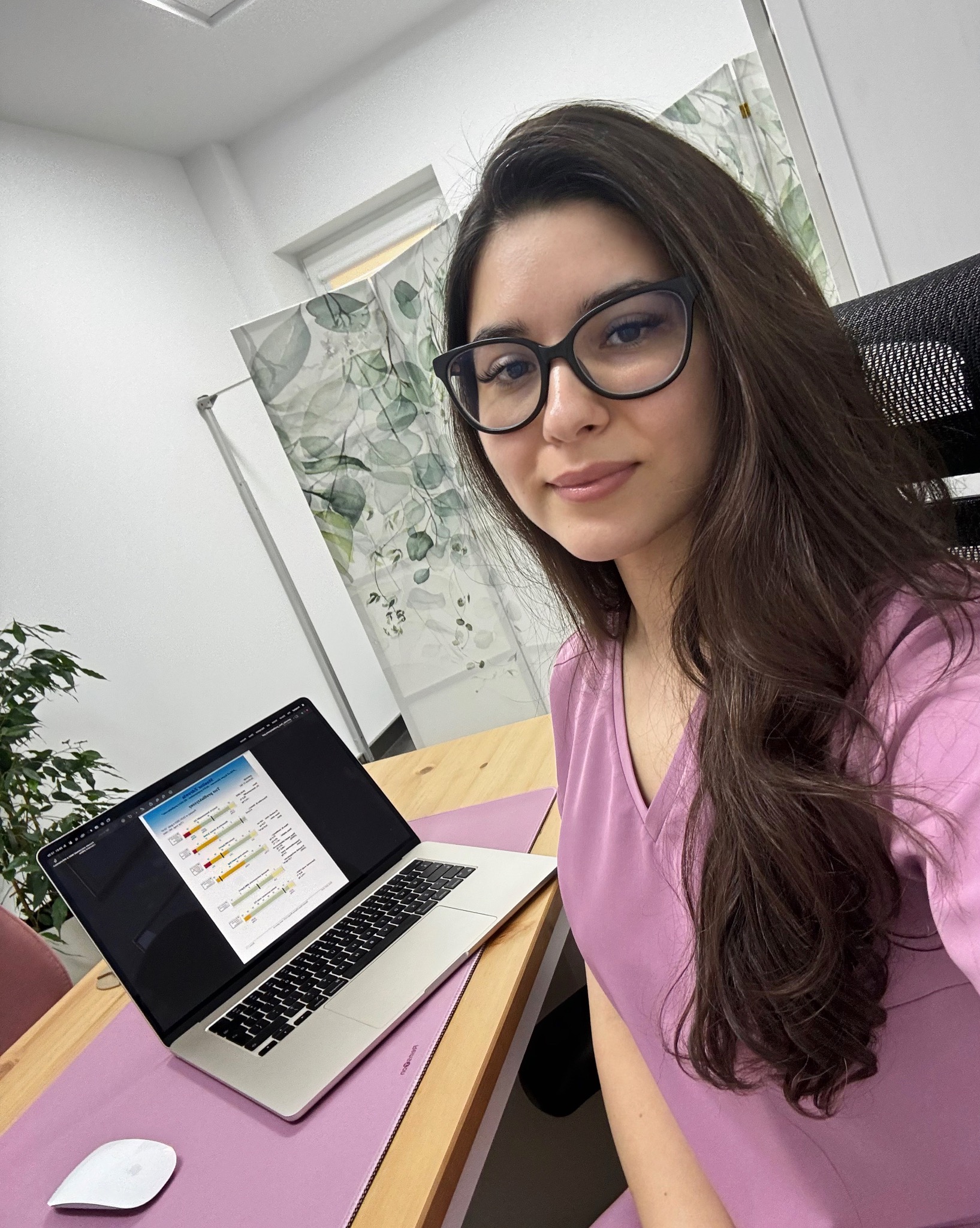 Dietetyk w okularach prezentuje na laptopie wyniki analizy składu ciała pacjenta, siedząc za biurkiem z fioletową podkładką.