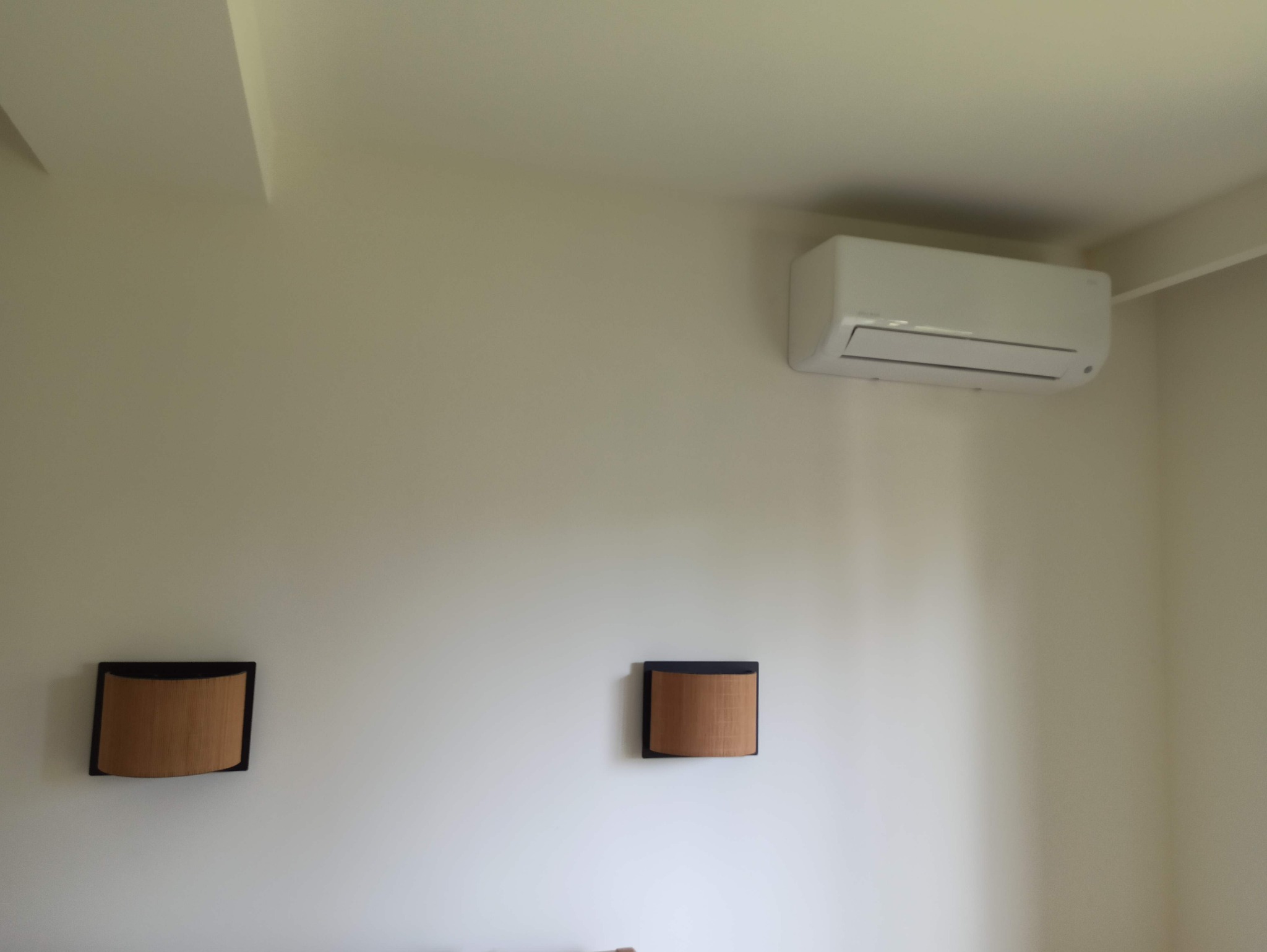 Biały klimatyzator ścienny zamontowany w jasnym pomieszczeniu z dwoma dekoracyjnymi panelami ściennymi z rattanu w ciemnych ramkach.