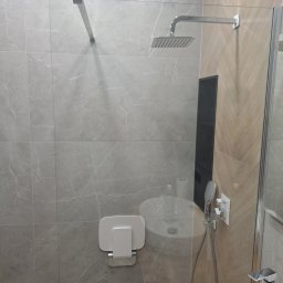 Igor tam - Nowoczesna kabina prysznicowa z deszczownicą i siedziskiem składanym, wykończona płytkami imitującymi marmur, z widoczną umywalką i baterią.