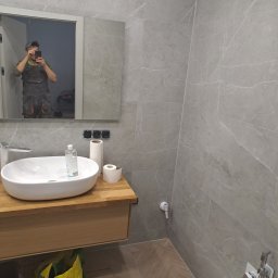 Igor tam - Nowoczesna łazienka z szarymi płytkami imitującymi marmur, drewnianą szafką pod umywalką i widocznym odbiciem osoby robiącej zdjęcie w lustrze.