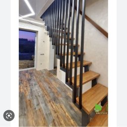 Igor tam - Nowoczesne schody drewniane z czarną balustradą, oświetlenie LED na suficie, widok na drzwi balkonowe z widokiem na zewnątrz.