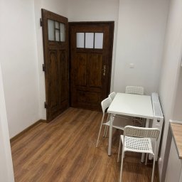 VS GROUPE OLEKSANDR PETRENKO - Wnętrze pokoju po remoncie: parkiet laminowany, odnowione drewniane drzwi z przeszkleniami, biały stół z krzesłami i grzejnik.