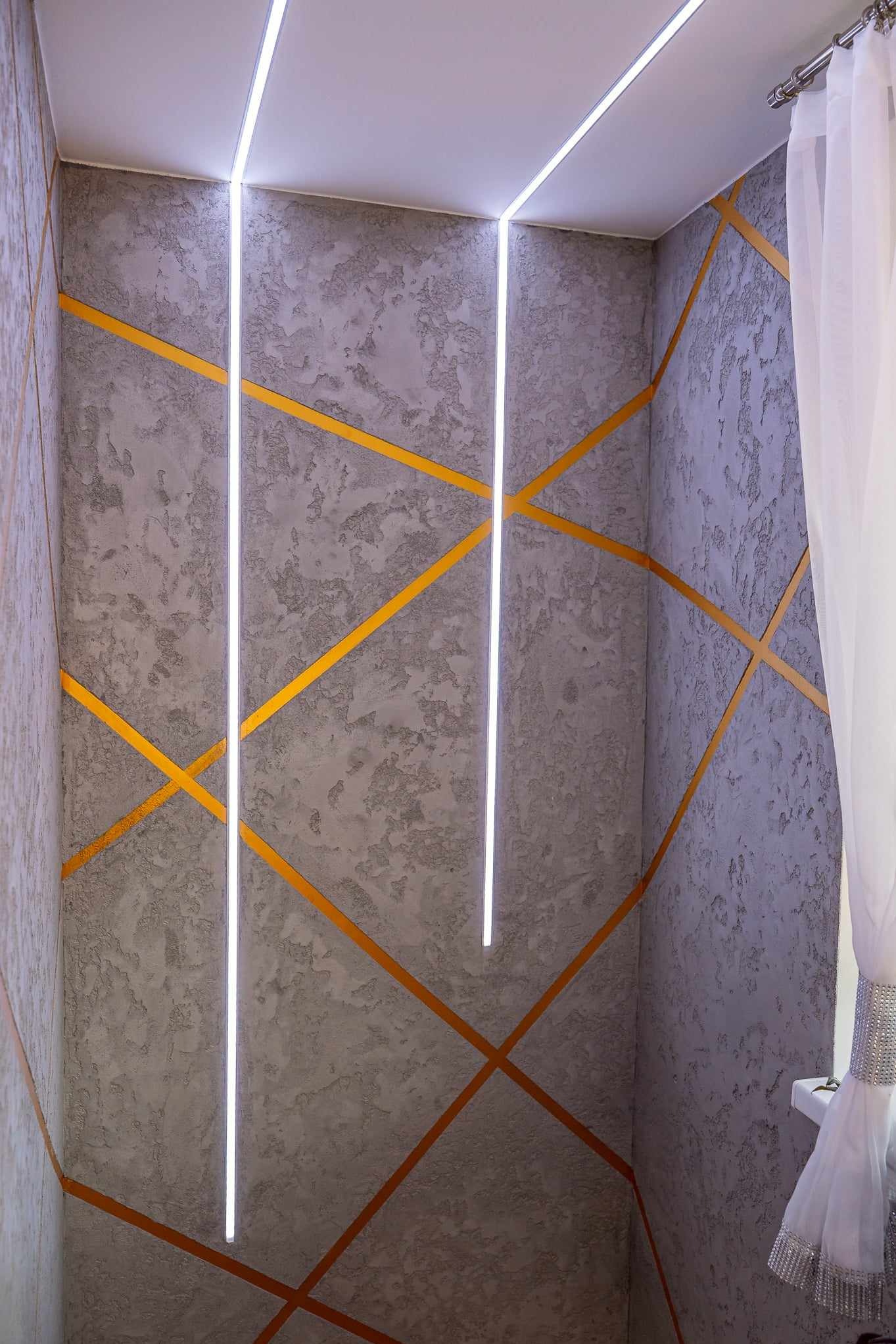 Nowoczesne wykończenie wnętrza: szpachlowana ściana w odcieniach szarości z geometrycznym wzorem z pomarańczowych pasów i pionowymi liniami oświetlenia LED.