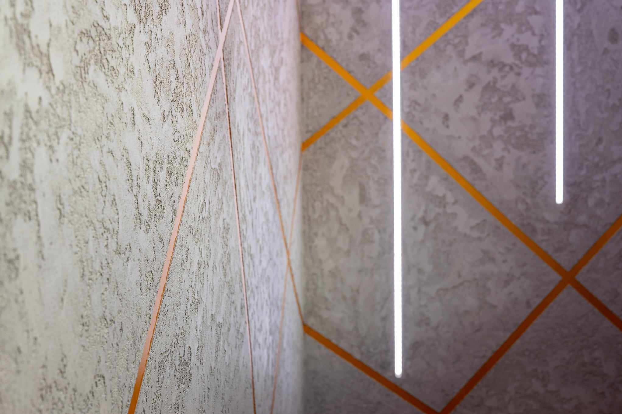 Teksturowana ściana w narożniku z dekoracyjnymi, pomarańczowymi paskami tworzącymi wzór rombów i pionową listwą LED.