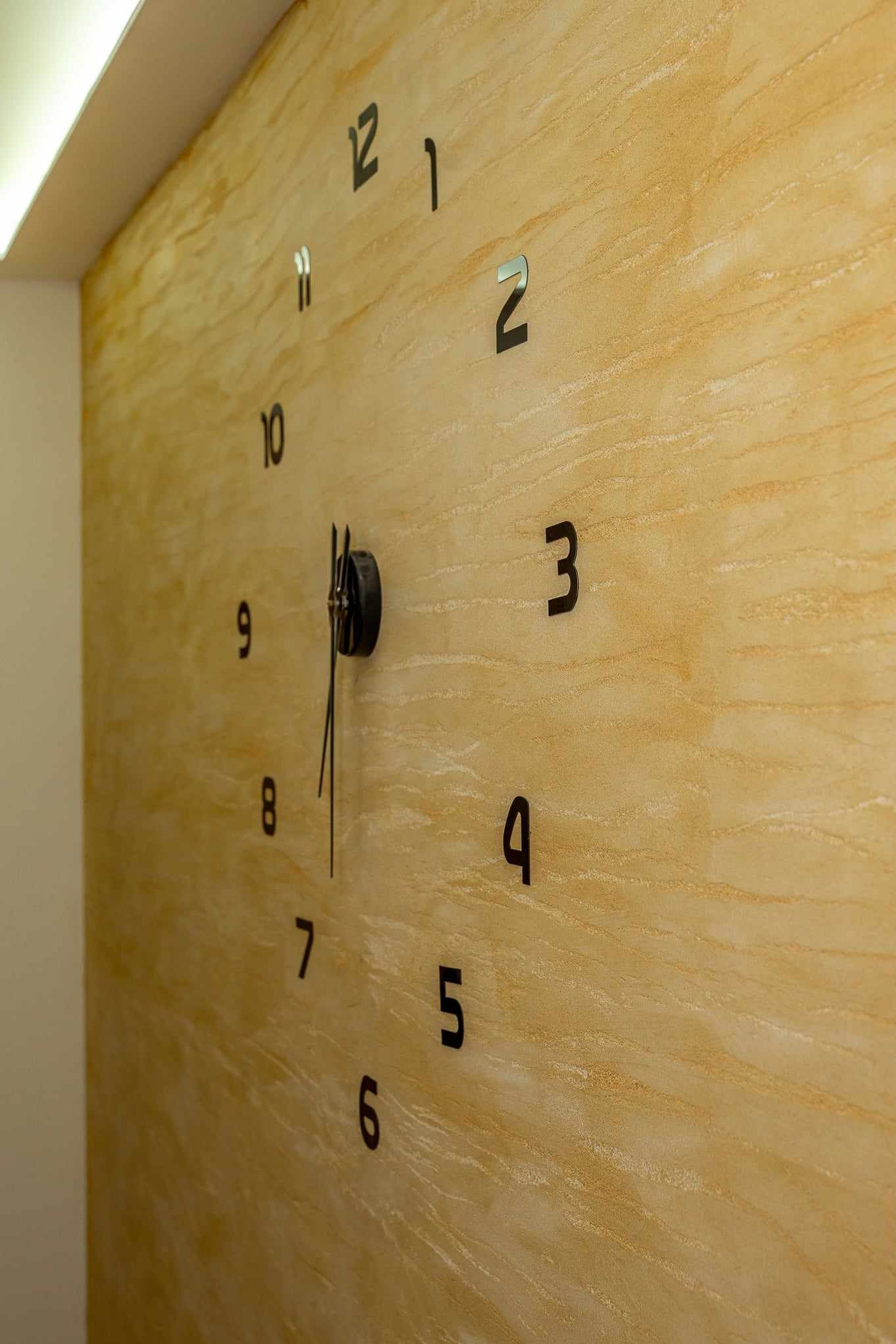 Dekoracyjna ściana z efektem piasku i zamontowany czarny zegar ścienny z minimalistycznymi cyframi.