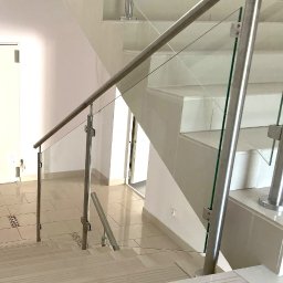 Loftowe-Design - Nowoczesna klatka schodowa z balustradą ze szkła i stali nierdzewnej, widok z góry na schody wyłożone jasnymi płytkami.