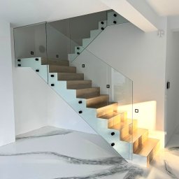 Loftowe-Design - Nowoczesne schody z drewnianymi stopniami i szklaną balustradą mocowaną punktowo, widok z dołu na marmurową posadzkę.