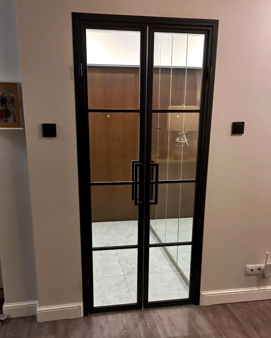 Dwuskrzydłowe drzwi z czarną ramą i szkłem, widok na wnętrze z jasną podłogą z płytek.