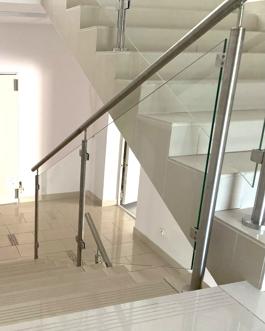 Nowoczesna klatka schodowa z balustradą ze szkła i stali nierdzewnej, widok z góry na schody wyłożone jasnymi płytkami.