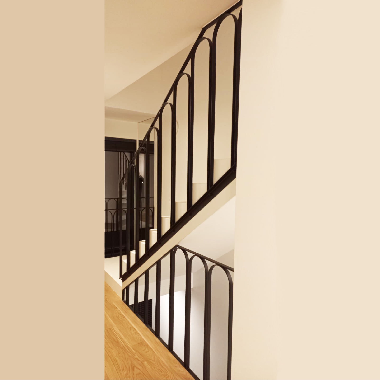 Minimalistyczna, czarna balustrada schodowa z pionowymi elementami w kształcie łuków, drewniane schody, jasne ściany.
