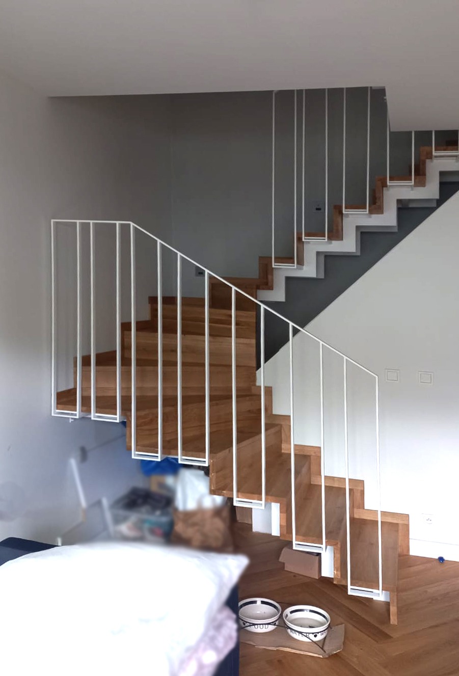 Drewniane schody z białą, minimalistyczną balustradą z pionowych prętów, widoczne dwa poziomy schodów, na podłodze miski dla zwierząt, w tle zagracone pomieszczenie.