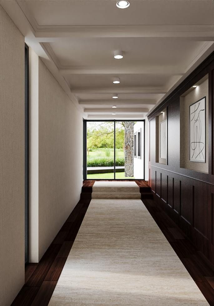 Długi korytarz z drewnianą podłogą i dywanem prowadzący do ogrodu. Ściany w jasnych odcieniach, oświetlenie punktowe. Po prawej stronie ciemne panele i obrazy.