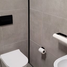 SAMIROL SPÓŁKA Z OGRANICZONĄ ODPOWIEDZIALNOŚCIĄ - Nowoczesna łazienka wykończona szarymi płytkami, z czarną armaturą, okrągłym lustrem i podwieszaną toaletą.