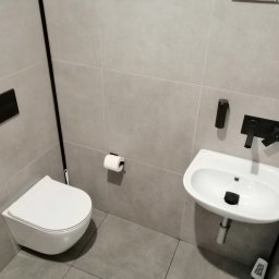 SAMIROL SPÓŁKA Z OGRANICZONĄ ODPOWIEDZIALNOŚCIĄ - Nowoczesna łazienka z szarymi płytkami, wiszącą toaletą i małą umywalką z czarną armaturą, minimalistyczny design.
