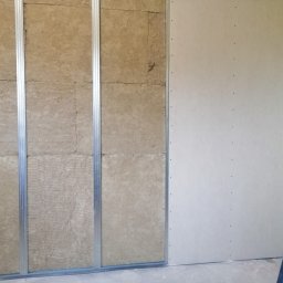 SAMIROL SPÓŁKA Z OGRANICZONĄ ODPOWIEDZIALNOŚCIĄ - Montaż izolacji z wełny mineralnej w metalowym stelażu pod płytę gipsowo-kartonową, widoczny poziomica oparta o ścianę.