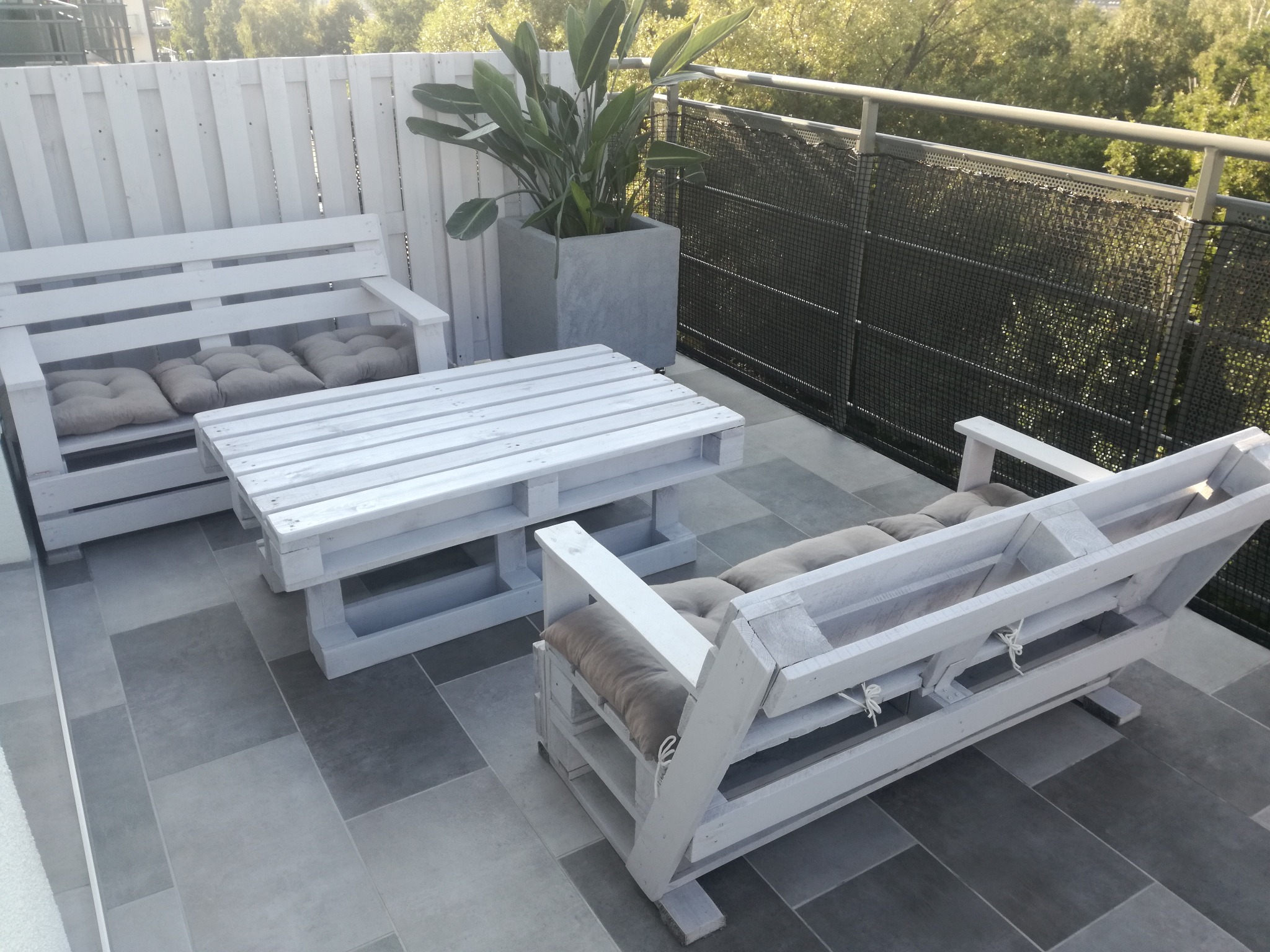 Białe meble ogrodowe z palet na balkonie z szarymi płytkami podłogowymi i rośliną w betonowej donicy