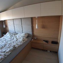 GKM MEBLE Sławomir Maciejczyk - Sypialnia z łóżkiem, szafkami nocnymi z szufladami i szafkami wiszącymi w zabudowie, oświetlenie punktowe, tapicerowany zagłówek w szarym kolorze, pościel w kwiatowy wzór.