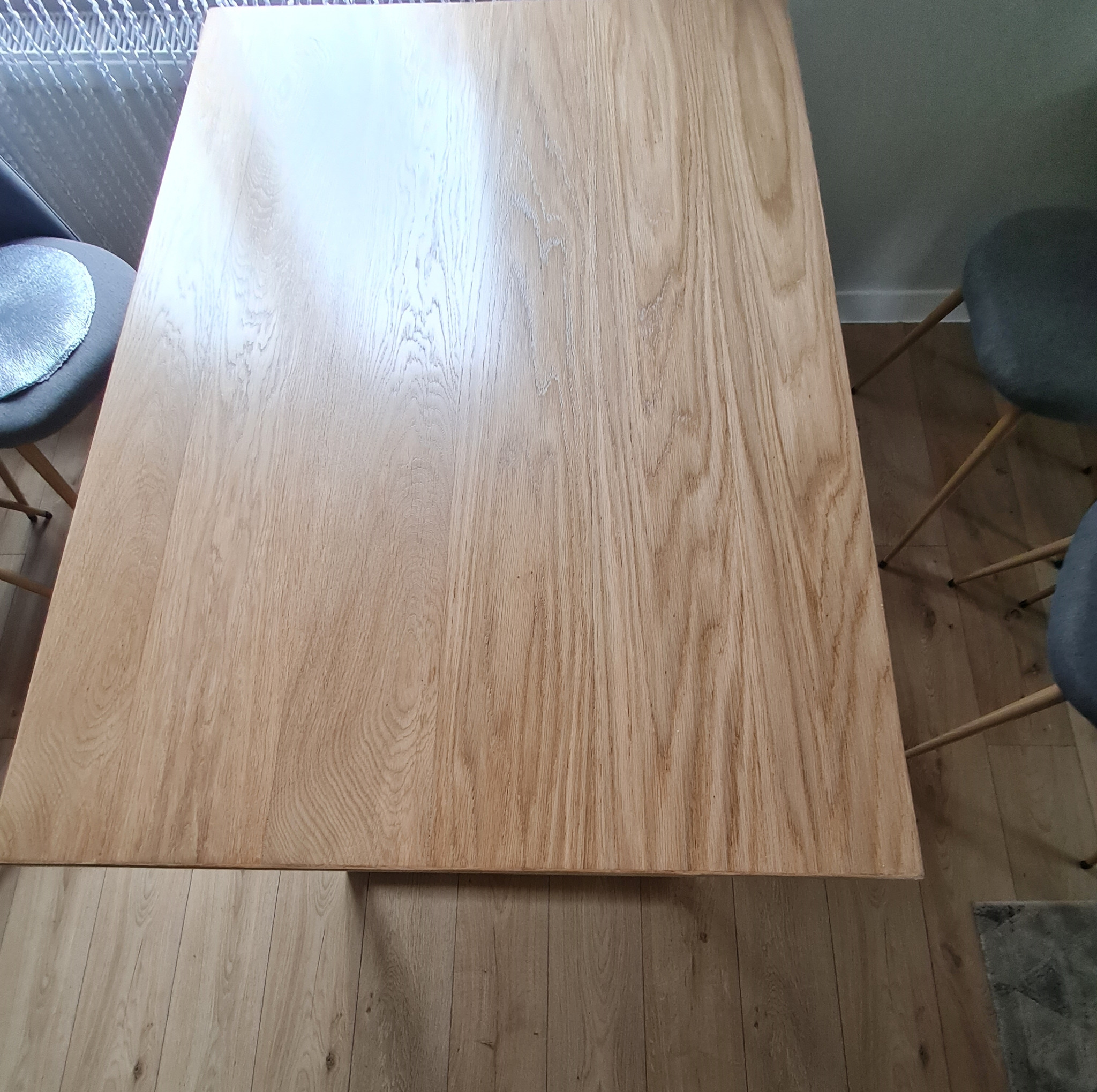 Dębowy stół z blatem o grubości 42mm, lakierowany na matowo, widziany z góry.  Widoczne krzesła i fragment parkietu. Naturalne światło podkreśla strukturę drewna.