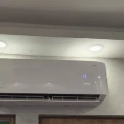 Biała klimatyzacja ścienna z wyświetlaczem temperatury 17 stopni Celsjusza, zamontowana na ścianie o szarej, teksturowanej tapecie w jasnym pomieszczeniu.