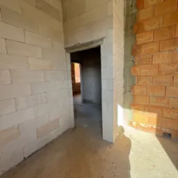 Wnętrze w trakcie budowy: ściany z betonu komórkowego i cegły ceramicznej, widoczne nadproże drzwiowe i fragment surowego stropu.
