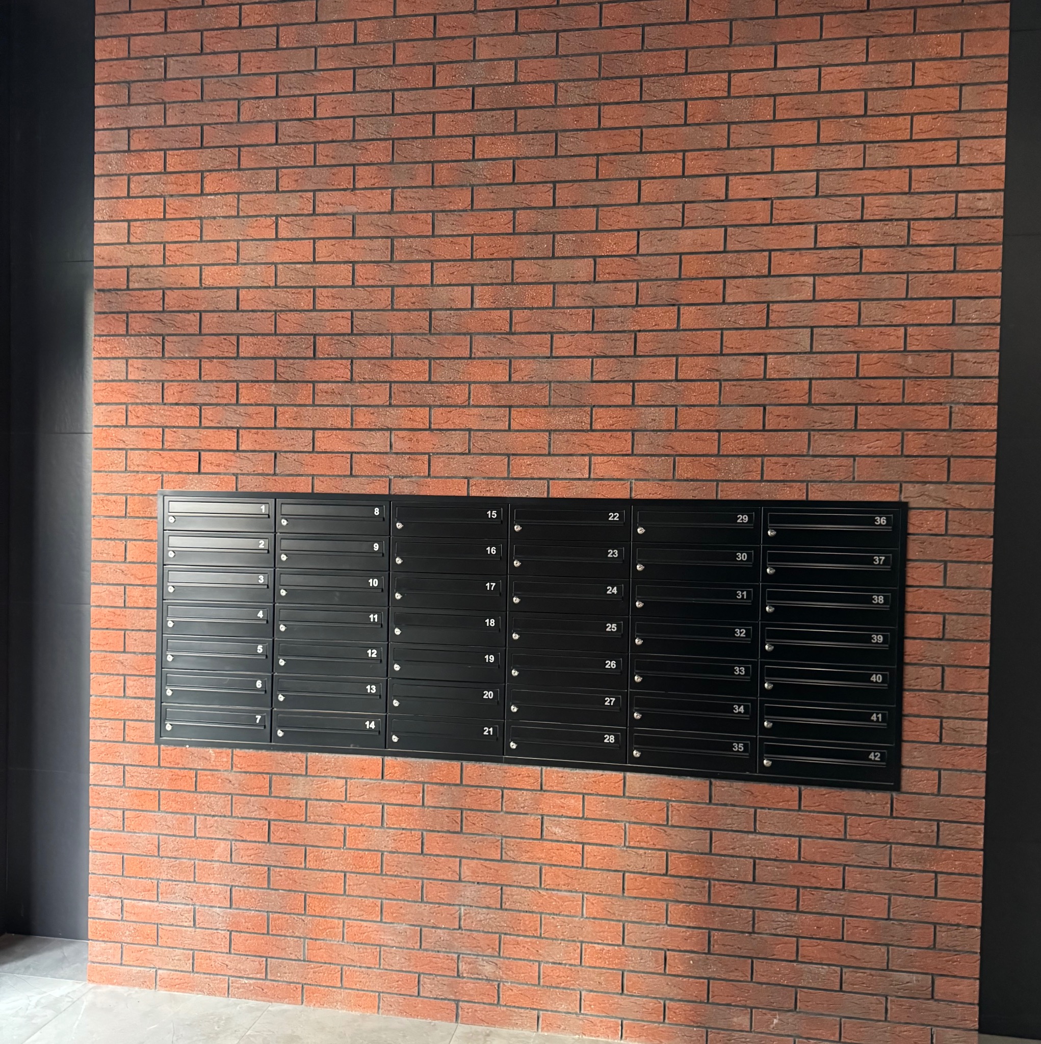 Czerwona ściana z cegły z zamontowanymi czarnymi skrzynkami pocztowymi numerowanymi od 1 do 42, widok z dołu.