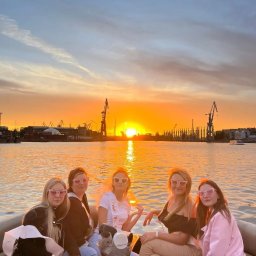 Yacht Club Premier - Grupa kobiet w okularach w kształcie serc świętuje na łodzi podczas zachodu słońca nad portem z dźwigami