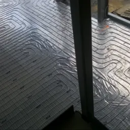 Rozłożona instalacja rur ogrzewania podłogowego na folii z rastrem, widok z góry na budowie, przygotowanie do zalewania wylewką.