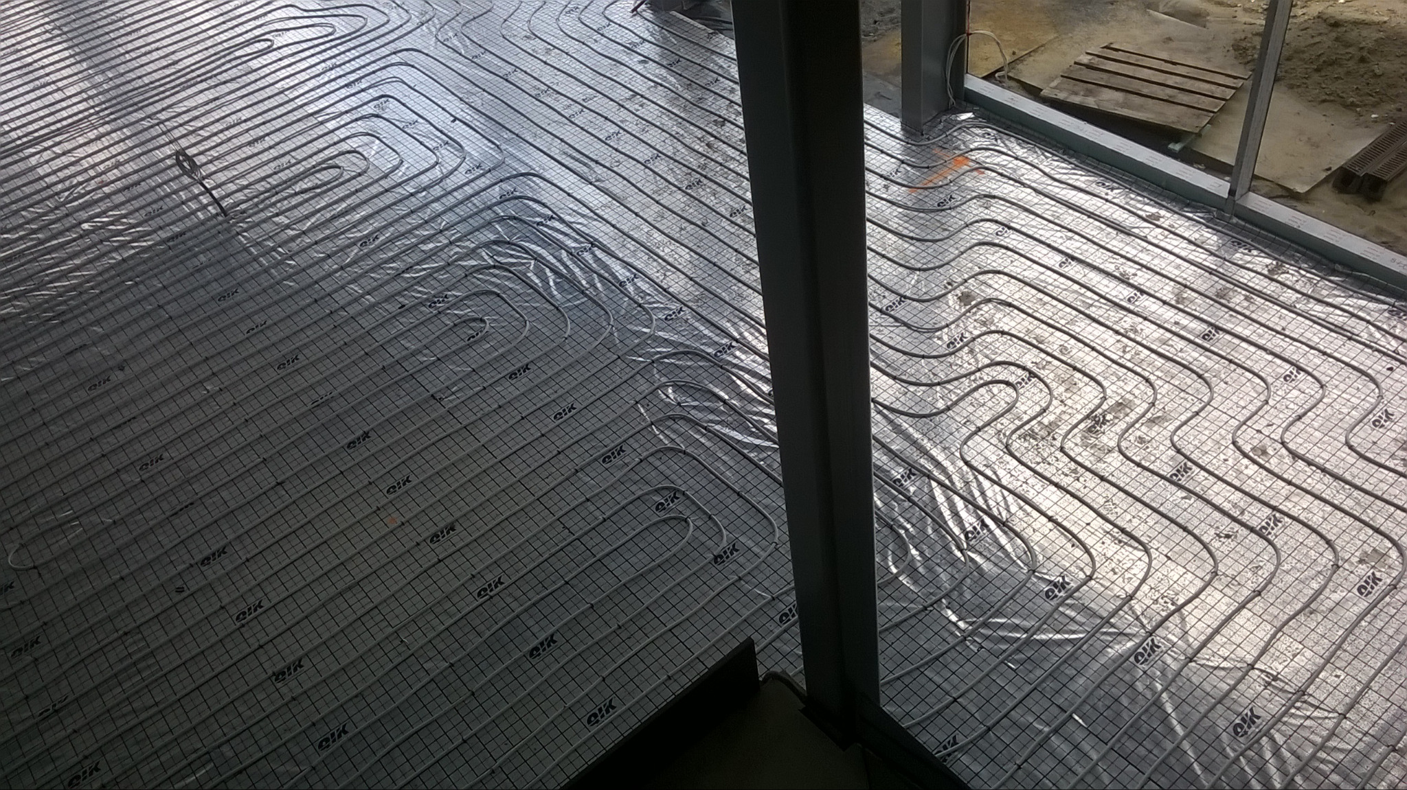 Rozłożona instalacja rur ogrzewania podłogowego na folii z rastrem, widok z góry na budowie, przygotowanie do zalewania wylewką.