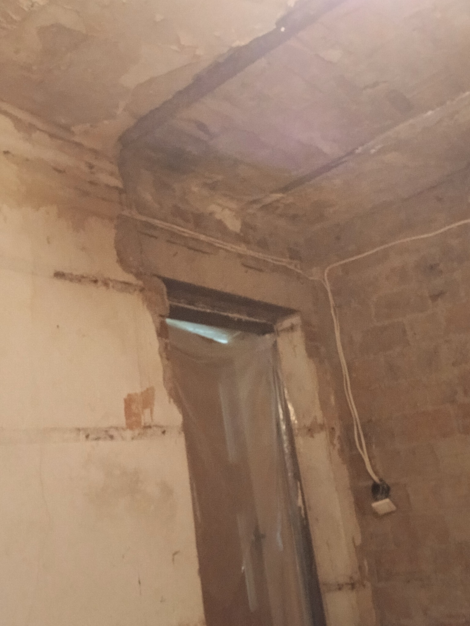 Niedokończone wnętrze z odsłoniętą konstrukcją sufitu i ścian, widoczne ślady po instalacjach, przygotowane do dalszych prac wykończeniowych. Kabel zwisa ze ściany.