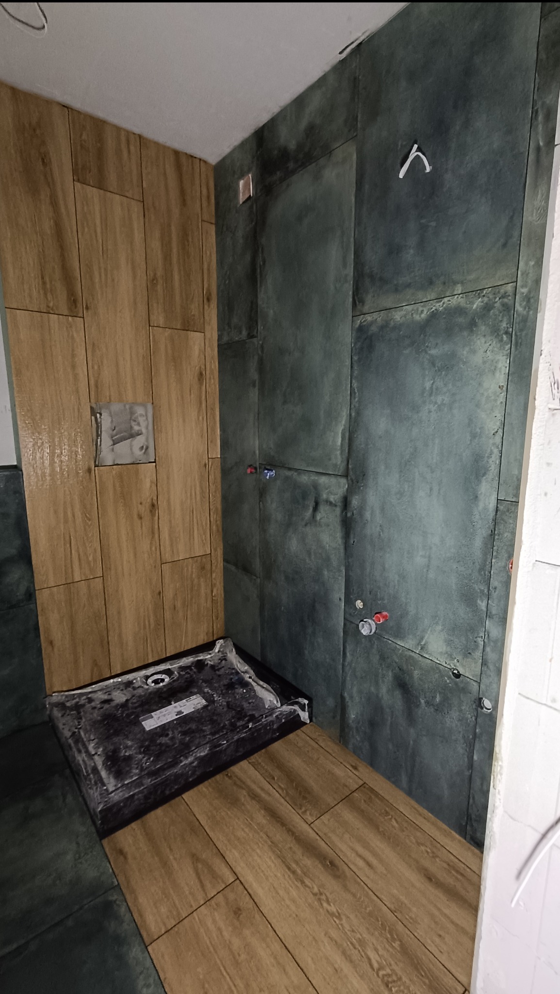 Montaż płytek w łazience: Połączenie drewnopodobnych i grafitowych płytek ściennych w trakcie instalacji brodzika.