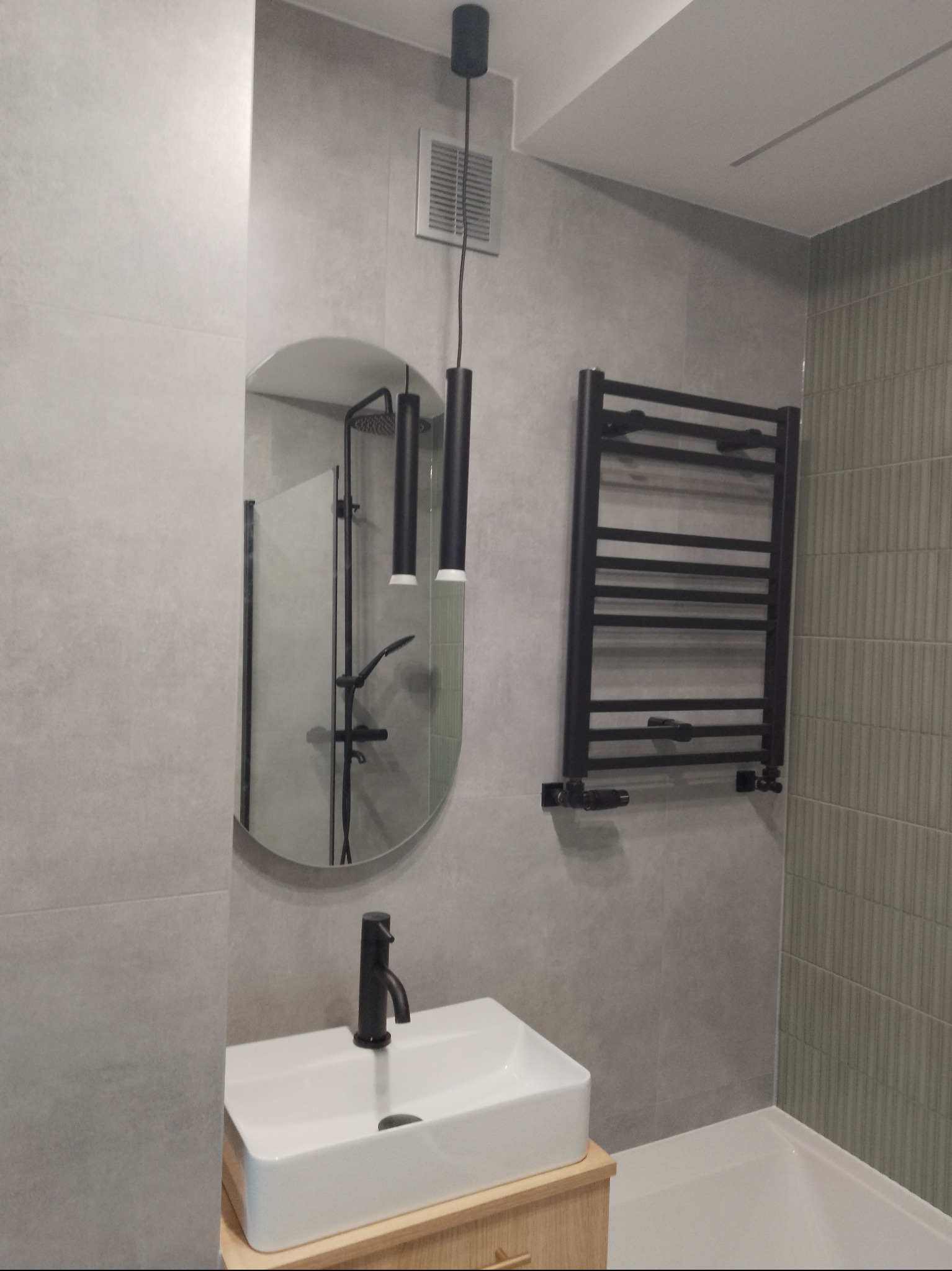 Nowoczesna łazienka w szarościach z owalnym lustrem, czarną armaturą i grzejnikiem drabinkowym. Minimalistyczny design, subtelne oświetlenie.