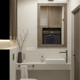 Minimalistyczna łazienka z ukrytą pralką za drewnianymi żaluzjami, umywalką nablatową, wiszącą toaletą i dekoracyjnymi gałązkami w wazonie.